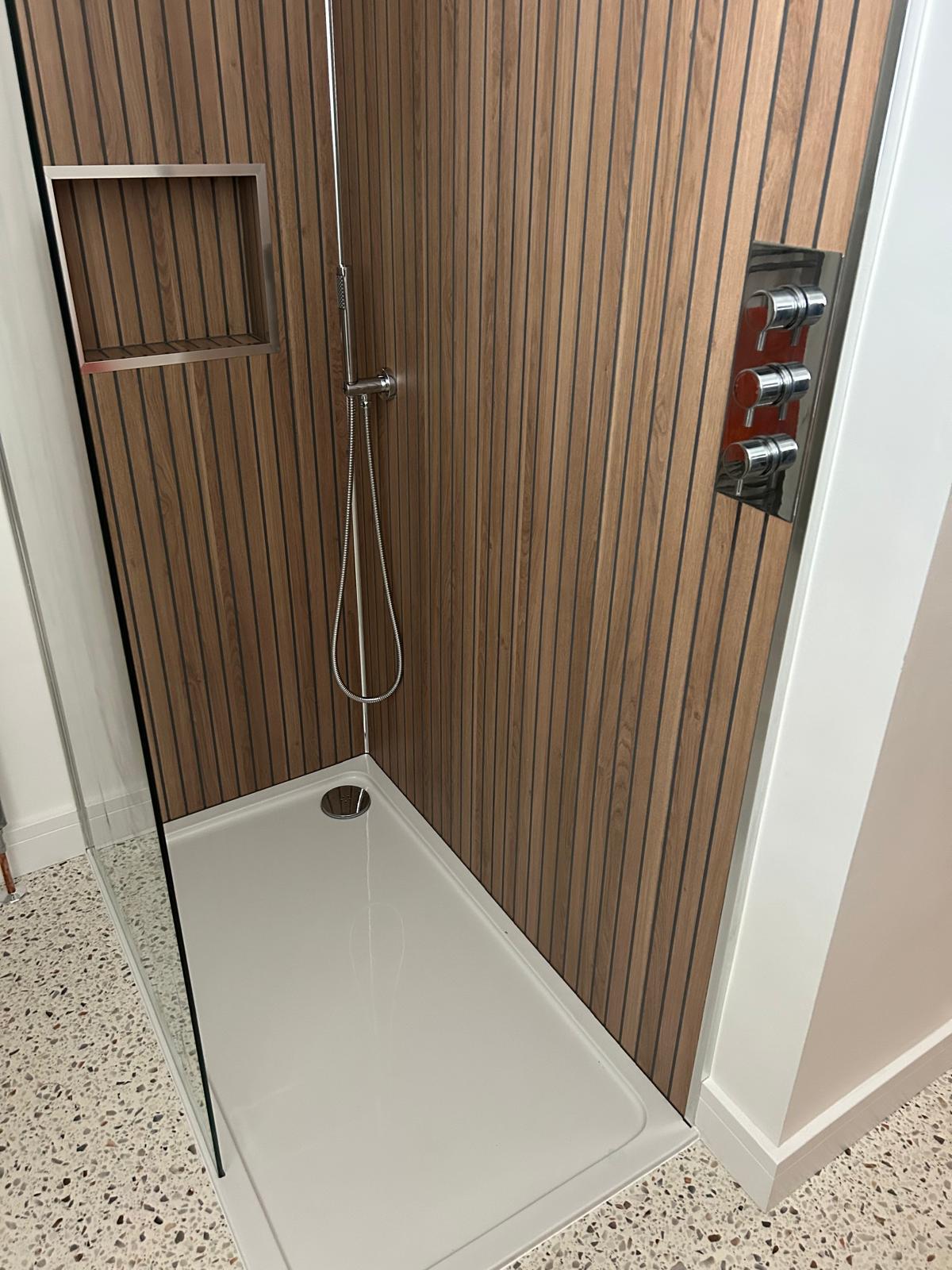 Walk-in shower with wood-panelled walls, recessed niche and glass screen