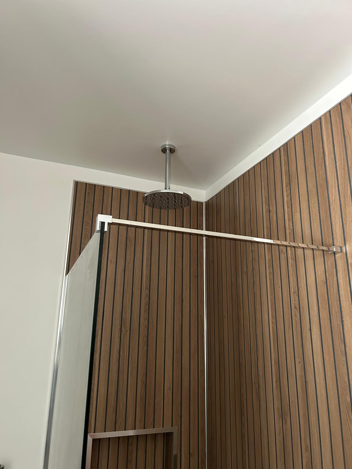 Ceiling-mounted rainfall shower head above the wood-panelled enclosure