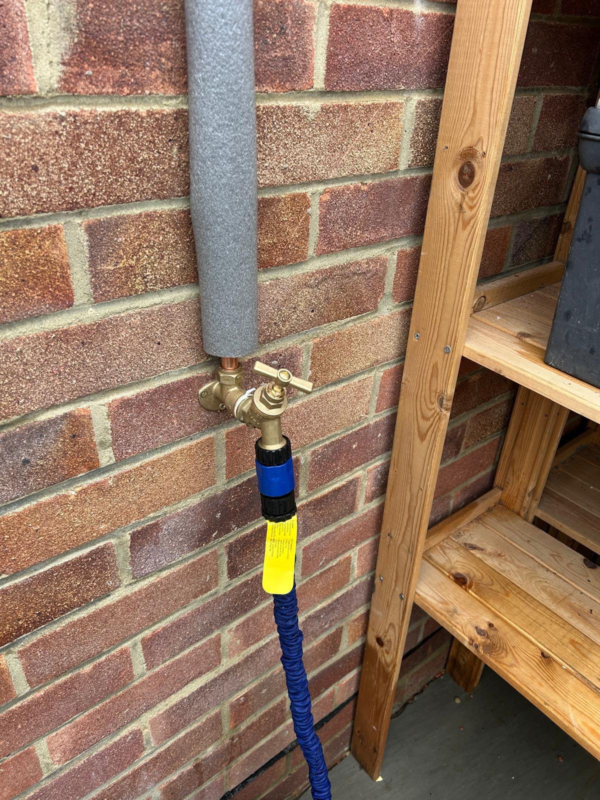 New brass outside tap with insulated supply pipe on a brick wall